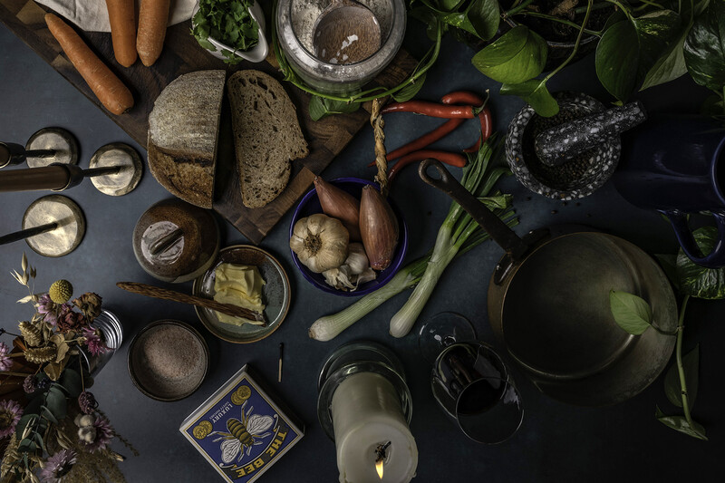 Flat lay arrangement of cooking ingredients and kitchen tools on dark surface.