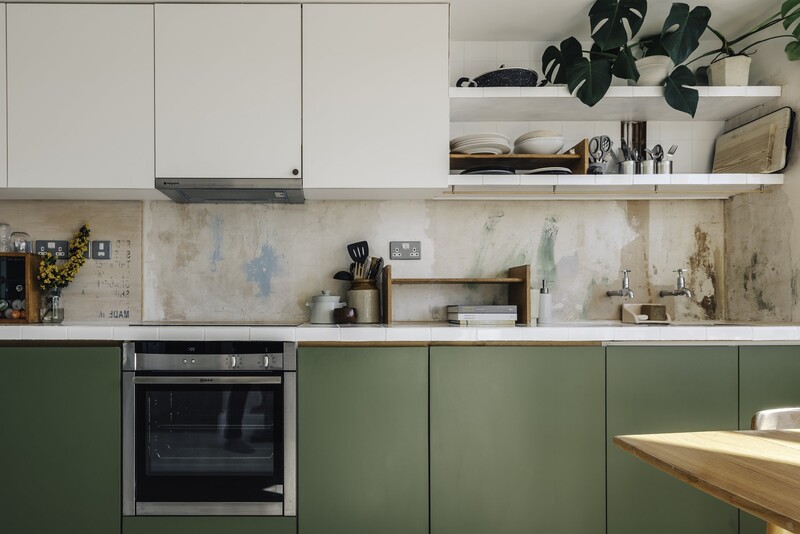 Modern kitchen with white upper cabinets, sage green lower cabinets, and weathered concrete backsplash.
