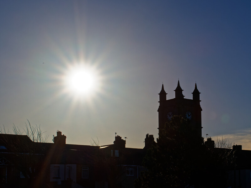 Silhouetted church with three spires against bright sun and blue sky.