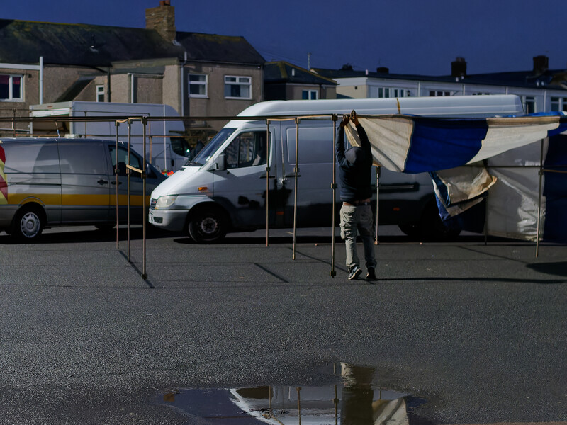 Person standing beside a white commercial van with an open awning in a parking lot during overcast daylight.