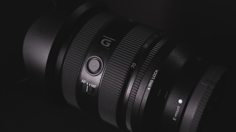 Sony G-series camera lens with focus ring and aperture markings in dramatic side lighting against a dark background.