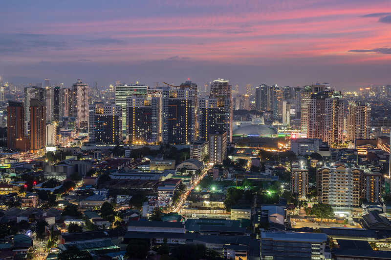 Urban skyline at dusk with illuminated high-rise buildings against a pink and purple twilight sky.