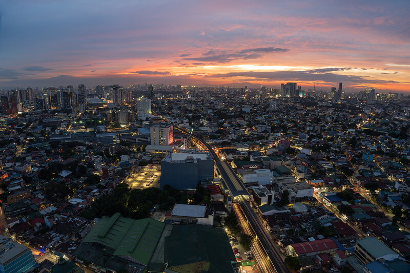 Aerial cityscape at twilight with illuminated streets, a central canal reflecting golden light, and dramatic sunset sky above.