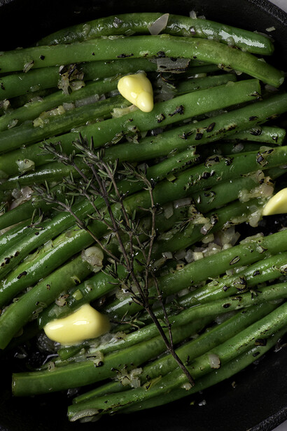 Green beans sautéed in a dark skillet with garlic cloves and fresh herbs.