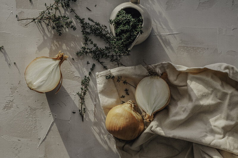 Flatlay composition of sliced and whole onions with fresh herbs on textured surface.