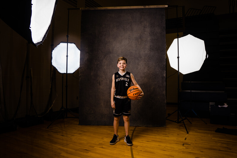 Young basketball player in black jersey holding an orange ball in a studio with softbox lighting.