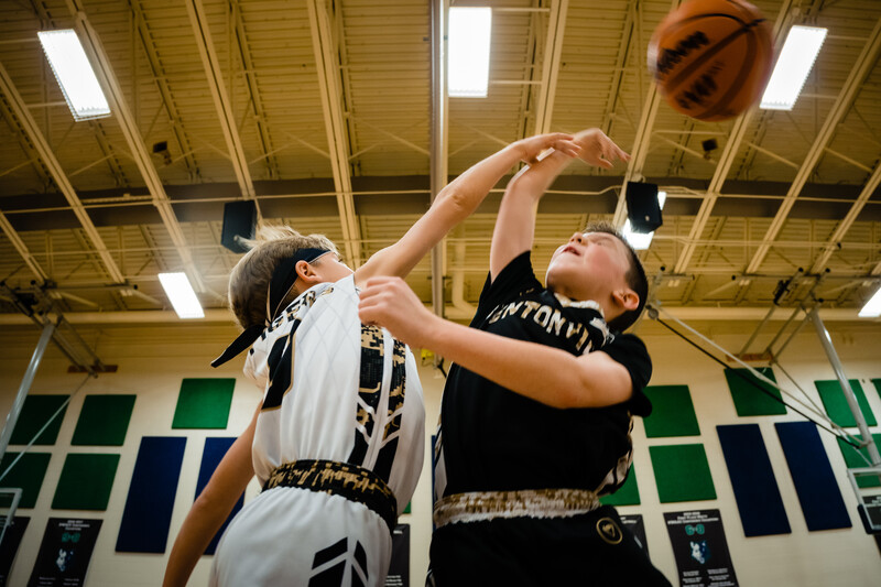 Two young basketball players jumping for a ball under gym lights.