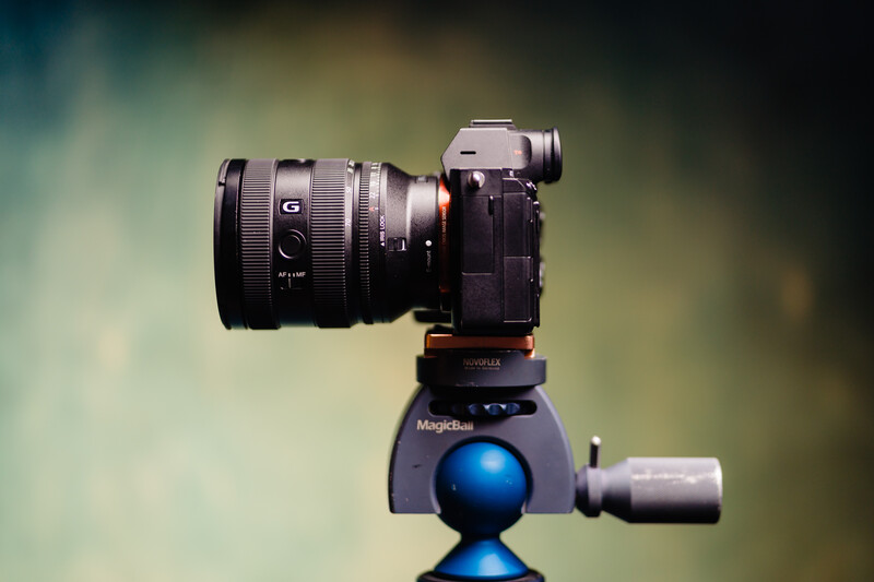 Sony mirrorless camera with wide-angle lens mounted on blue ball head tripod against blurred background.