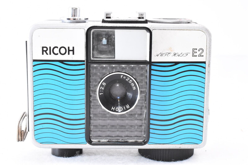 Ricoh half-frame film camera with white body and turquoise wave pattern design.