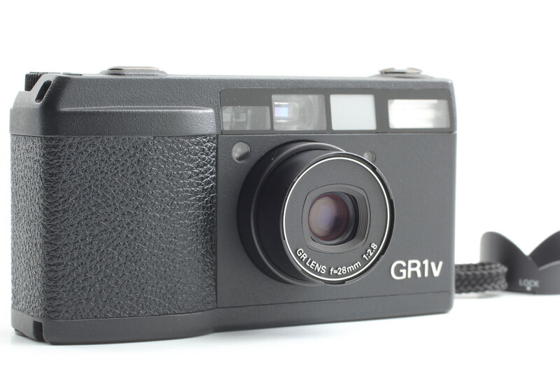 Ricoh GR IV compact camera with textured grip, shown at three-quarter angle with shoulder strap attached.