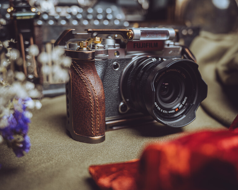 Vintage rangefinder camera with brown leather grip and attached light meter, surrounded by colorful flowers.