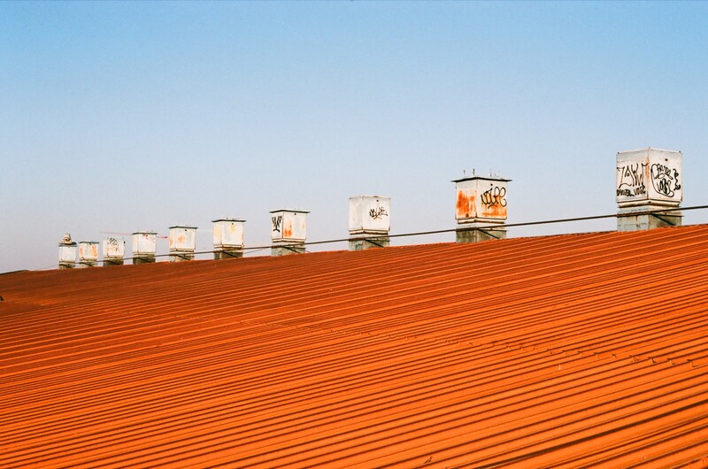 Row of white and orange industrial ventilation units lined along a bright orange corrugated metal roof against clear blue sky.