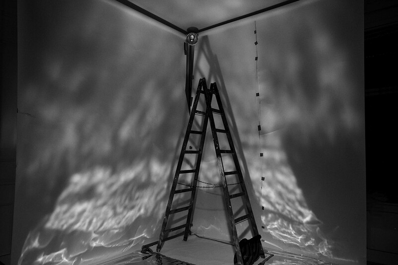 Ladder leaning against corner wall with dramatic shadow patterns in black and white.