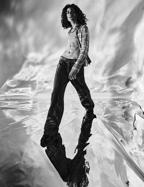 Person standing in dramatic black and white portrait with their reflection visible below.