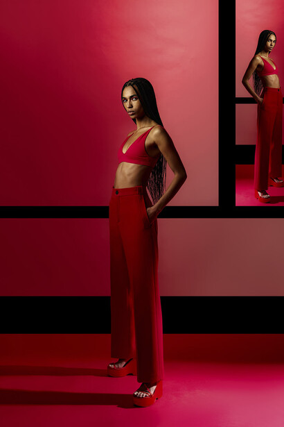 Woman in red crop top and matching pants posed against geometric red and black wall backdrop.