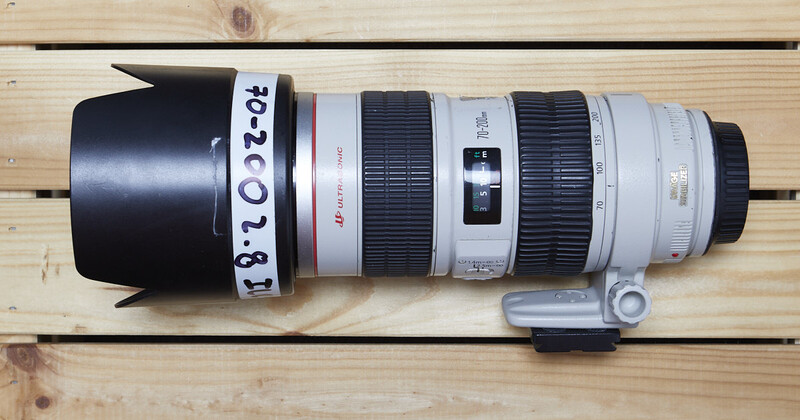 Canon telephoto zoom lens with lens hood and serial number tag on wooden surface.