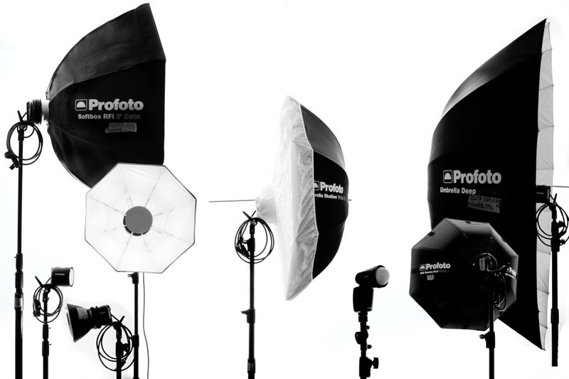Professional studio lighting kit with three Profoto strobe heads, octagonal and parabolic softboxes, and light stands arranged in a flat lay composition.