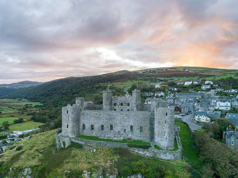 Medieval stone castle with multiple towers overlooking a hillside town and green valley at dusk.