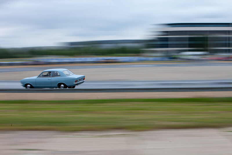 Blue sedan captured with panning motion blur against stationary background elements.