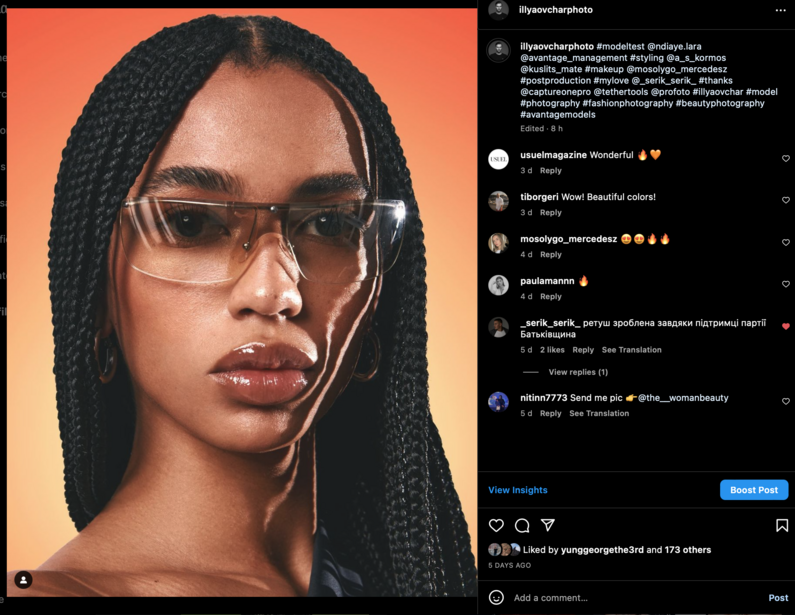 Portrait of a woman wearing oversized transparent-frame glasses against a warm orange gradient background.
