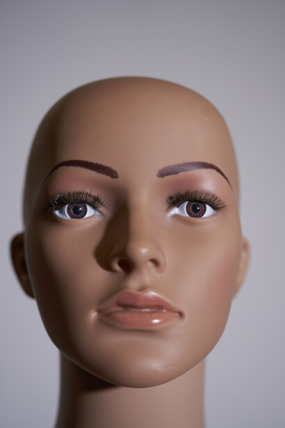 Close-up portrait of a realistic mannequin head with neutral expression and directional lighting.