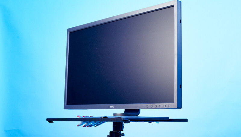 Professional monitor mounted on an articulating arm against a blue background.