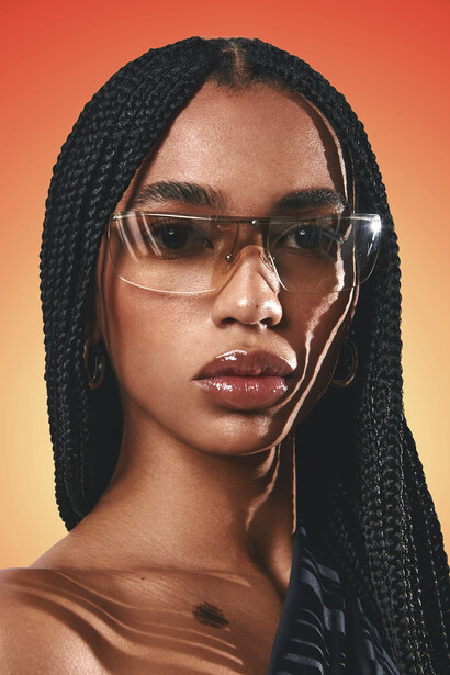 Portrait of a person wearing clear-framed glasses and earbuds against a warm orange gradient background.