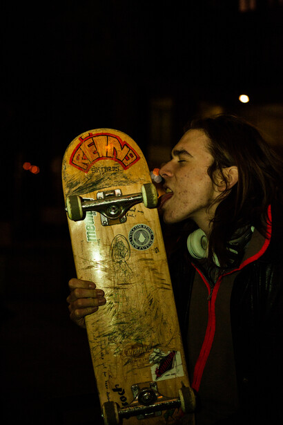 Man with dreadlocks kissing a worn skateboard deck at night.