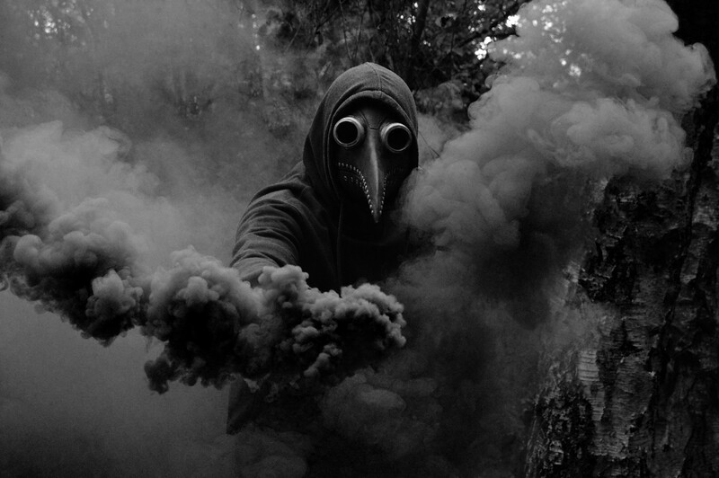 Figure wearing plague doctor mask surrounded by billowing smoke in monochromatic composition.