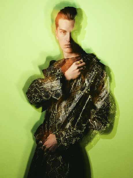 Man in gold sequined jacket against bright lime green background with soft vignette.