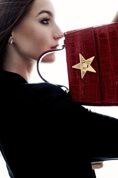 Woman in profile holding red textured wallet with gold star detail against white background.