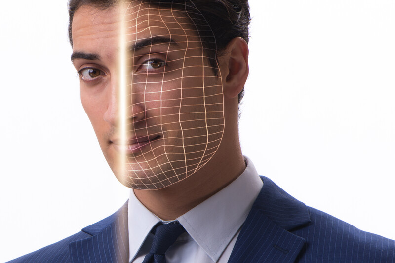 Professional man in business suit with digital facial recognition grid overlay on half his face.