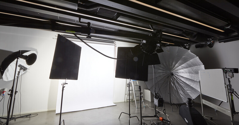Professional photography studio with overhead lighting rigs, softboxes, and reflectors suspended from ceiling tracks.