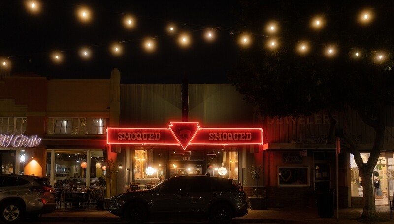 Neon-lit storefront at night with red triangular sign and warm overhead string lights.