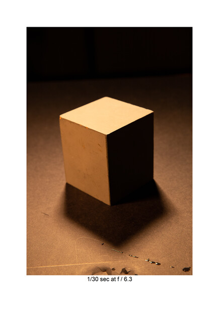 Three-dimensional rendered cube with warm and cool lighting creating strong shadows on a textured surface.