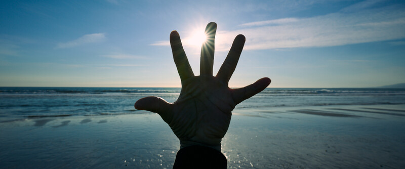 Silhouetted hand raised against bright sun and ocean horizon.
