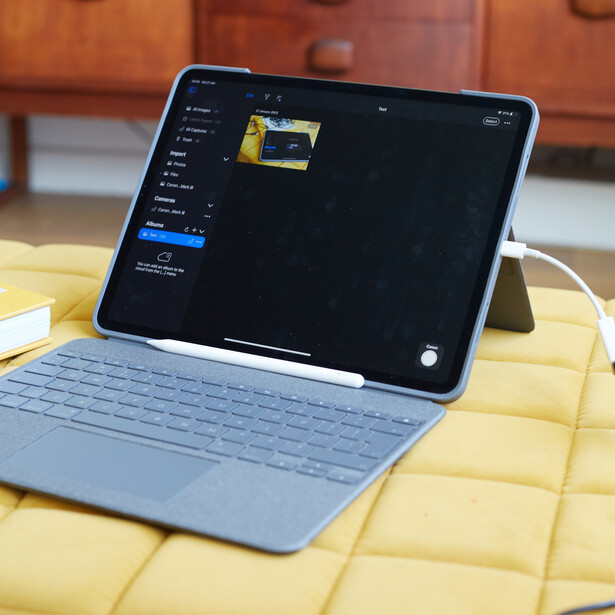 iPad and light blue keyboard case displayed on a yellow quilted surface, showing dark editing software interface on screen.