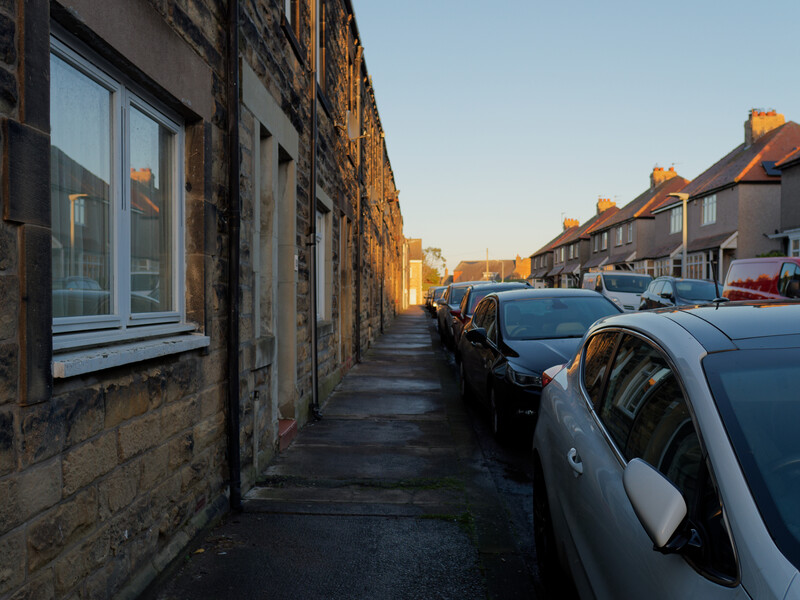 Row of parked cars along a narrow residential street lined with stone buildings during golden hour.