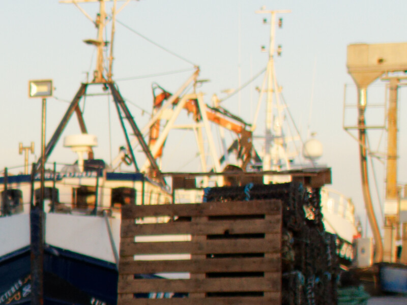 Industrial fishing vessel with cargo cranes and rigging against golden hour light.