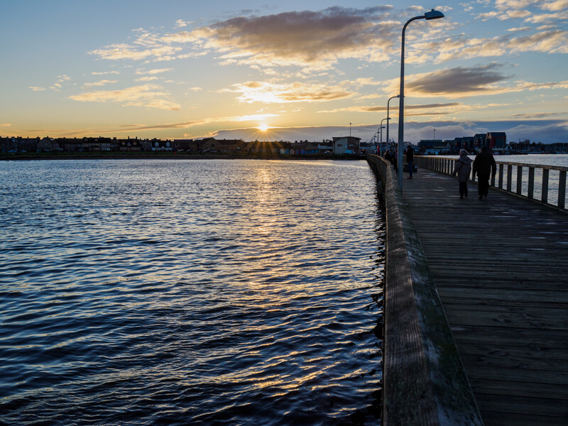 Long wooden pier extending into calm water at sunset with golden light reflecting off the surface.