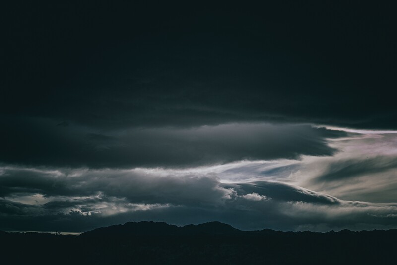 Dramatic storm clouds with sunlit edges over a dark mountainous landscape silhouette.