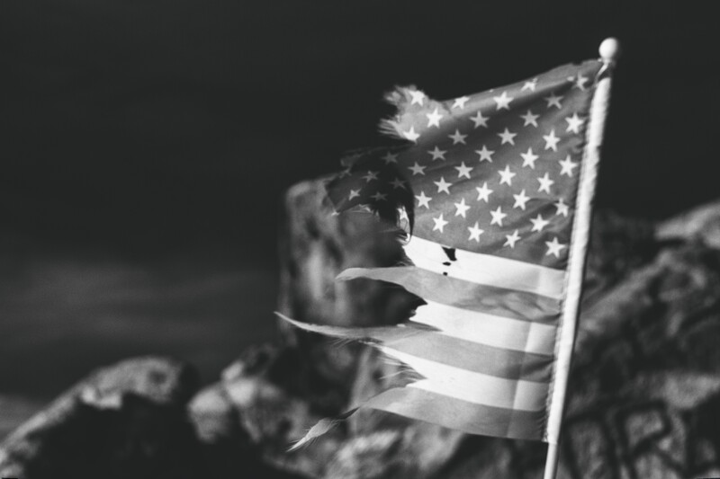 American flag held by a soldier in black and white, with blurred background and dramatic lighting.