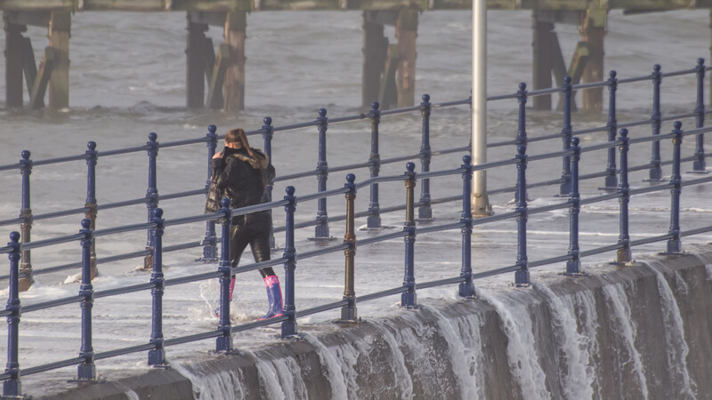 Runner jogging along a waterfront promenade with metal railings and wooden pilings visible.