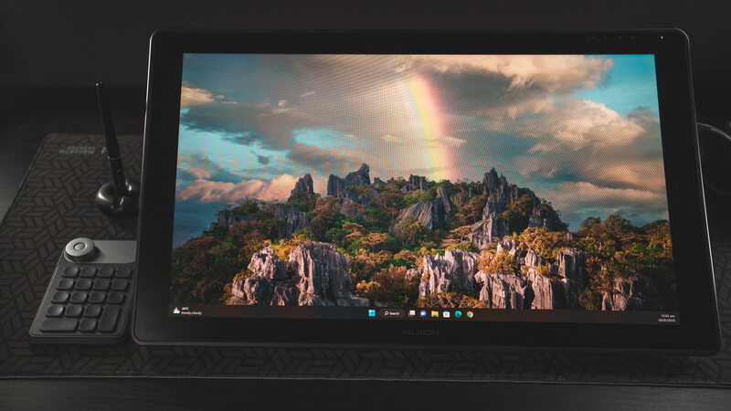 Landscape photograph displayed on a tablet showing a mountainous island with dramatic rainbow and sunset sky.