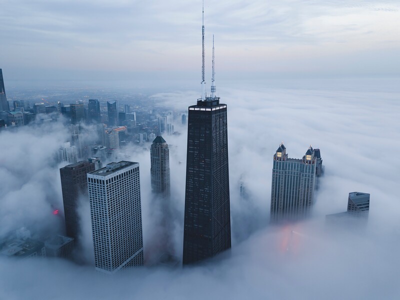 Downtown skyscrapers rising above a thick blanket of fog at dusk.