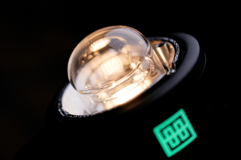 Glass dome light with warm tungsten glow against black background with neon green square.