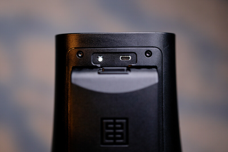 Close-up of black device rear showing USB port, power button, and maker's emblem against blurred background.