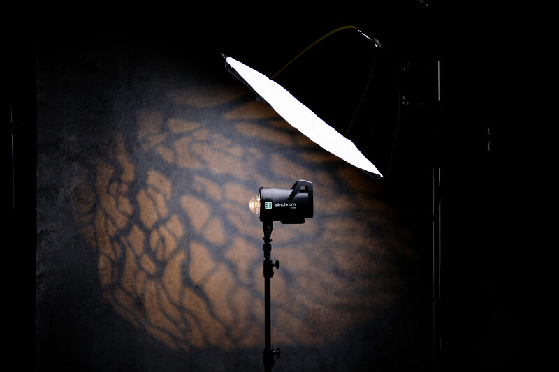 Studio lighting setup with a spotlight on a stand casting dramatic shadows on a textured background.