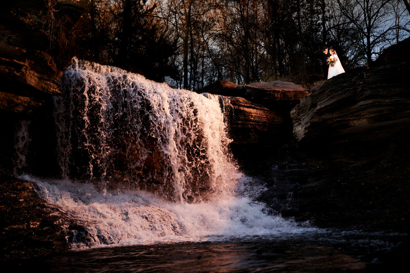 Waterfall cascading over rocky ledge with golden sunlight illuminating the falling water and mist.