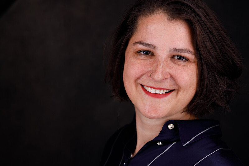 Woman with shoulder-length dark hair smiling at camera against dark background.
